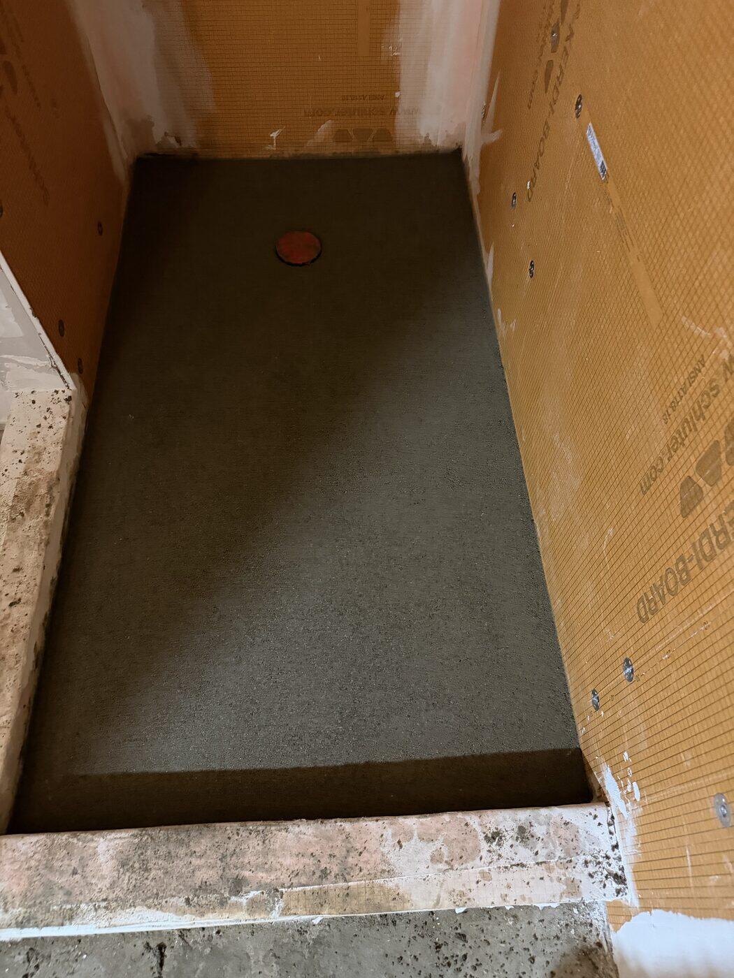A shower pan floated inside orange waterproof board and sloped toward a round drain.